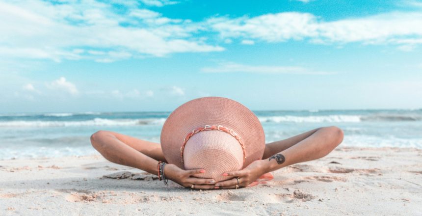 vacationer lying on a beach with a sun hat on