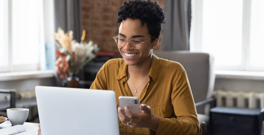 African,Woman,Sit,At,Workplace,Desk,Holds,Cellphone,Staring,At